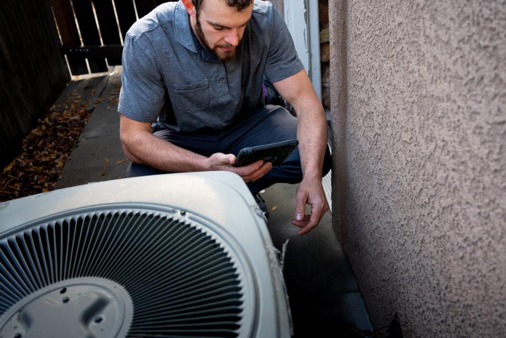 年轻的男性物业督察在一幢粉刷过的房屋旁拍摄一条通往住宅空调冷凝器的线路